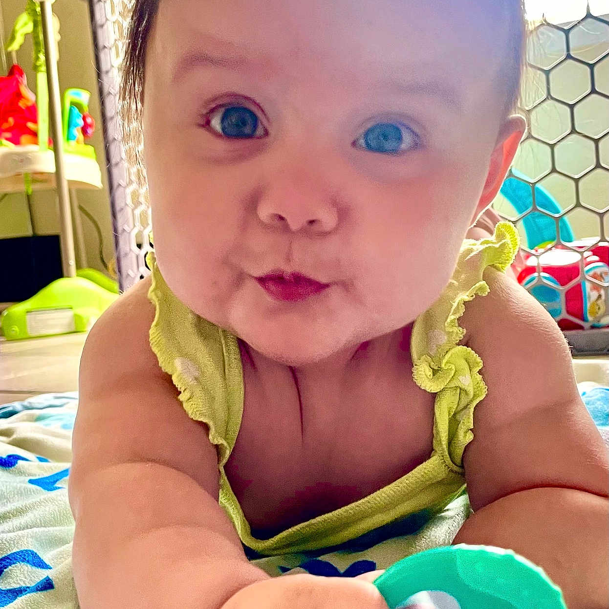 Emery is registered to the contest to win money with this photo: baby, blanket, blue_eyes, child, chubby_cheeks, closeup, colorful, curious, cute, expression, face, floor, green_clothing, hand, indoors, infant, play_area, plaything, safe_environment, teething_toy