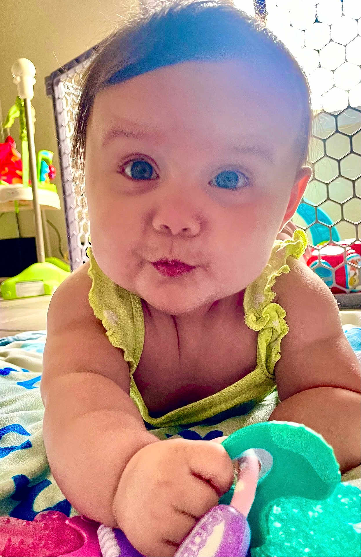 Emery is registered to the contest to win money with this photo: baby, infant, child, teething_toy, blanket, play_area, curious, cute, indoors, closeup, face, hand, blue_eyes, green_clothing, plaything, chubby_cheeks, expression, floor, colorful, safe_environment