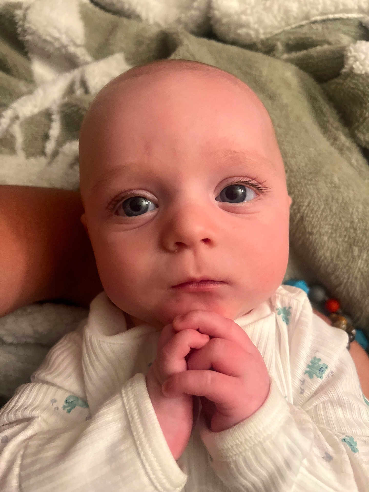 Bodie is registered to the contest to win money with this photo: baby, infant, face, hands, clothing, white, blue_eyes, close_up, portrait, skin, expression, cute, child, newborn, person, soft, blanket, sleepwear, resting, indoors