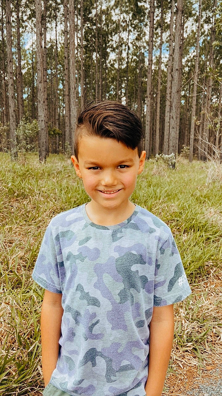 Elijah is registered to the contest to win money with this photo: botany, child, electric_blue, eye, facial_expression, grass, hairstyle, happy, joy, leaf, mammal, people_in_nature, person, plant, sleeve, smile, standing, summer, t_shirt, tree