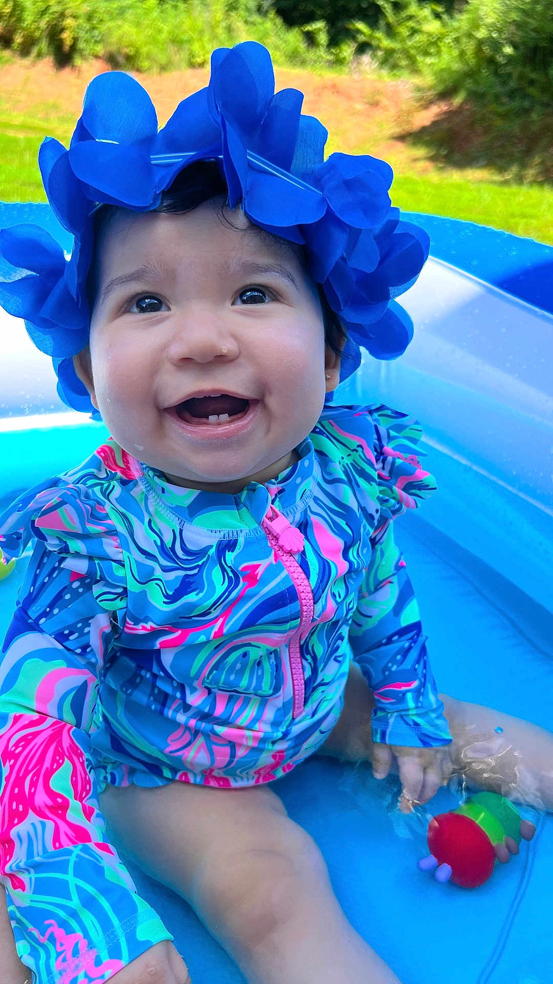 Amy joined the competition — help win amazing prizes! baby, child, smiling, pool, water, toy, swimsuit, blue, flower_hat, outdoor, summer, splashing, happy, cute, infant, playing, colorful, sunny, nature, grass