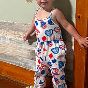 Olivia is registered to the contest to win money with this photo: barefoot, blonde_hair, casual, child, clothing, cute, home, indoor, jumpsuit, person, pigtails, playful, smiling, standing, toddler, toy_bottle, usa_theme, wooden_floor, wooden_wall, young_child