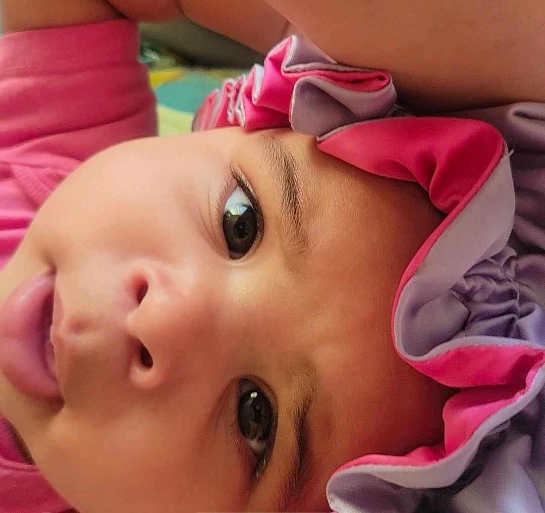 Claire joined the competition — help win amazing prizes! baby, close_up, face, headband, pink, purple, tongue, cute, child, curious_eyes, infant, playful, portrait, skin, young_child, lying_down, expression, soft_lighting, indoors, headwear