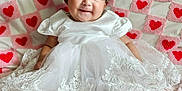 Merida is registered to the contest to win money with this photo: baby, infant, smile, white_dress, lace, cute, child, portrait, soft_blanket, pink, hearts, quilt, happy, indoors, candid, socks, black_hair, bow, sitting, cozy