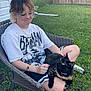 Millie joined the competition — help win amazing prizes! person, cat, glasses, chair, outdoor, grass, fence, wicker_chair, shorts, tortoiseshell_cat, sitting, relaxed, daylight, backyard, casual_clothing, greenery, pet, summer, nature, happy