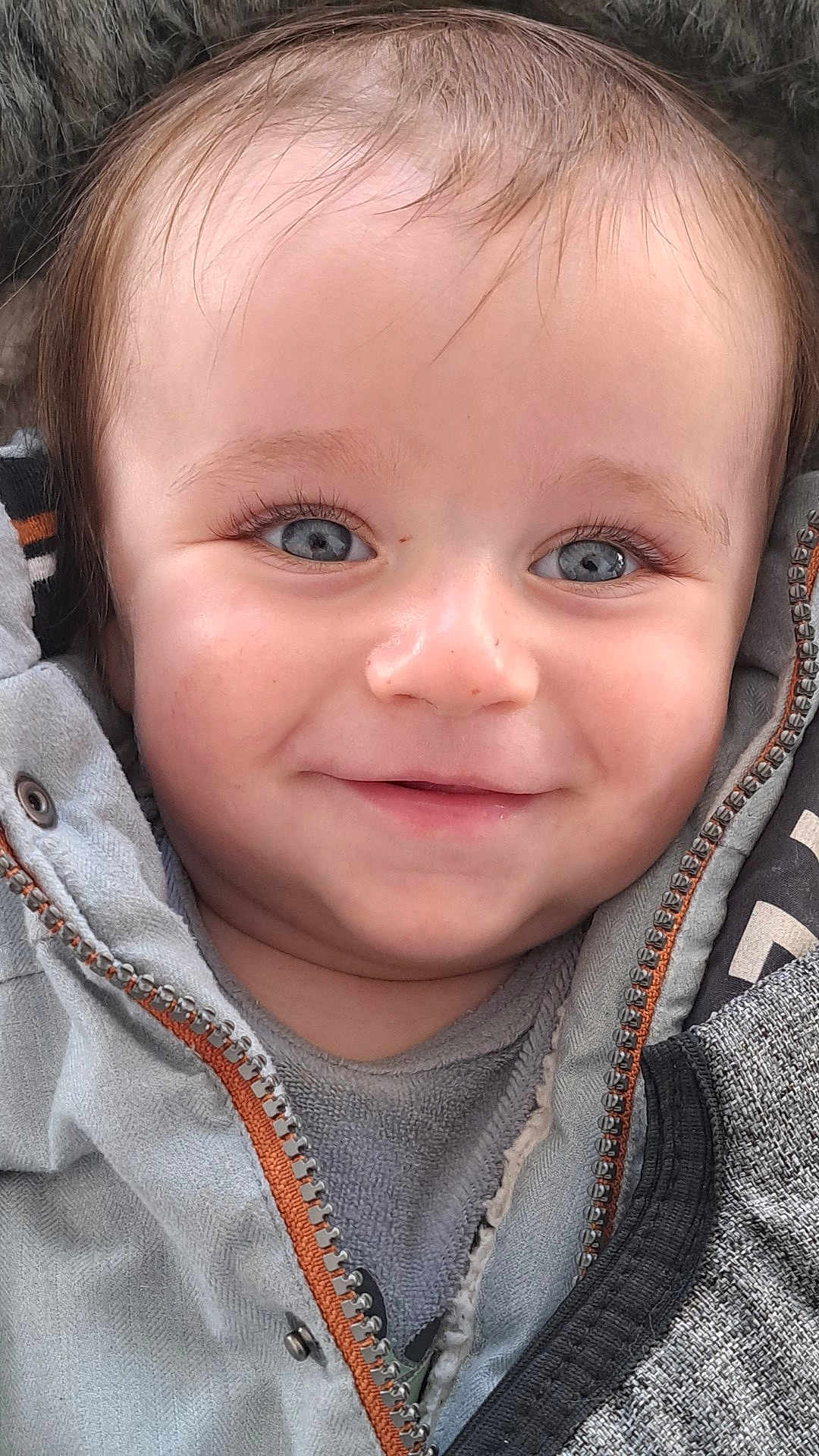 Ethan a rejoint le concours — aidez-le/la à gagner de superbes lots ! baby, infant, smiling, blue_eyes, long_eyelashes, jacket, zipper, hood, close_up, portrait, skin, hair, cheeks, mouth, nose, eyebrows, clothing, fabric, cozy, happy