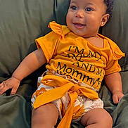 Nola joined the competition — help win amazing prizes! baby, child, smiling, yellow_shirt, white_socks, bow, indoor, couch, green_couch, happy, cute, infant, portrait, sitting, clothing, person, home, relaxed, skin, legs