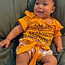 baby, child, smiling, yellow_shirt, white_socks, bow, indoor, couch, green_couch, happy, cute, infant, portrait, sitting, clothing, person, home, relaxed, skin, legs