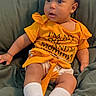 baby, child, infant, sitting, couch, yellow_clothing, white_socks, bow, curly_hair, indoor, portrait, cute, expression, comfortable, young_child, person, home, soft_fabric, casual, relaxed