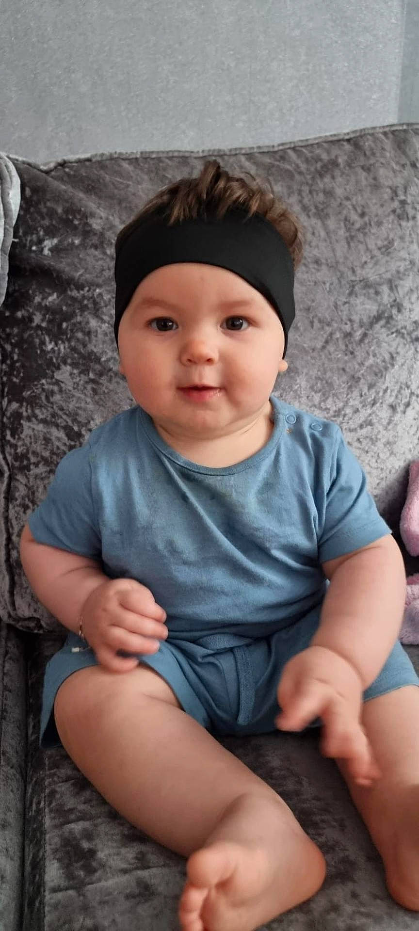 baby, barefoot, blue_clothing, casual_clothing, child, comfortable, couch, curly_hair, cute, face, hands, headband, indoor, infant, legs, plush, portrait, sitting, smiling, young_child
