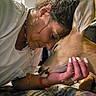 affection, bed, bedroom, blanket, brown_dog, close_up, dog, face, floppy_ears, hand, human, indoors, jewelry, kissing, pet, portrait, sunlight, white_shirt, window, woman