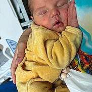 Lyzio a rejoint le concours — aidez-le/la à gagner de superbes lots ! baby, newborn, sleeping, yellow_onesie, hand, person, cozy, soft_texture, indoor, closeup, infant, cute, resting, human, child, tender, comfort, portrait, peaceful, cuddle