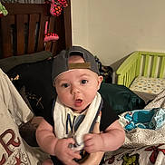 Forrestt is registered to the contest to win money with this photo: baby, infant, cap, bib, person, holding, indoor, bedroom, crib, blanket, stuffed_toy, wooden_furniture, expression, curious, child, adult_arm, clothing, facial_expression, home, baby_supplies