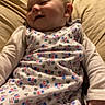 baby, infant, sleepwear, pillow, smile, child, indoors, cute, relaxing, patterned_clothing, face, sleeping_bag, home, soft_light, young_child, person, comfort, candid, portrait, resting