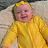 baby, infant, yellow_outfit, headband, bow, smile, happy, blanket, soft_texture, lying_down, cute, child, indoor, portrait, face, small_hand, cheeks, eyes, clothing, warm_colors