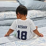 Keshav joined the competition — help win amazing prizes! child, toddler, baby, sitting, back_view, bedroom, bed, bedding, pillow, blanket, jersey, number_18, striped_clothing, dark_hair, indoor, home, pacifier, bracelet, photography, portrait