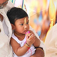 Keshav joined the competition — help win amazing prizes! toddler, child, baby, portrait, sitting, indoors, celebration, family, adult, man, traditional_clothing, white_clothing, black_hair, facial_mark, bracelets, necklace, pink_toy, hands, colorful_background, candid
