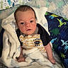 Zane joined the competition — help win amazing prizes! baby, infant, child, portrait, sitting, wide_eyed, indoors, bed, blanket, bedding, dinosaur_pattern, football_shirt, clothing, fluffy_blanket, home, nursery, cute, face, photography, cozy
