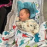 baby, infant, sleeping, bassinet, blanket, dinosaur_pattern, blue_plush, nursery, portrait, cozy, indoors, lying_down, peaceful, newborn, clothing, bedding, crib, face, resting, colorful