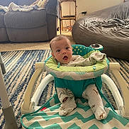 Zane joined the competition — help win amazing prizes! baby, child, infant, indoor, living_room, activity_walker, sitting, wide_eyed, open_mouth, portrait, onesie, clothing, carpet, rug, couch, bed, blanket, furniture, home, colorful