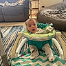baby, child, infant, indoor, living_room, activity_walker, sitting, wide_eyed, open_mouth, portrait, onesie, clothing, carpet, rug, couch, bed, blanket, furniture, home, colorful