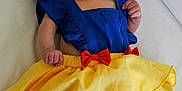 Hope a rejoint le concours — aidez-le/la à gagner de superbes lots ! baby, infant, costume, dress, blue_top, yellow_skirt, red_bow, apple, fruit, lying_down, white_background, curious, hand, foot, face, head, skin, newborn, child, cute