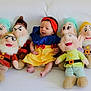 baby, child, plush_toys, snow_white_costume, dwarfs, stuffed_animals, couch, white_background, costume, headband, sitting, soft_toys, colorful, indoor, cute, portrait, infant, smiling, playful, fairy_tale