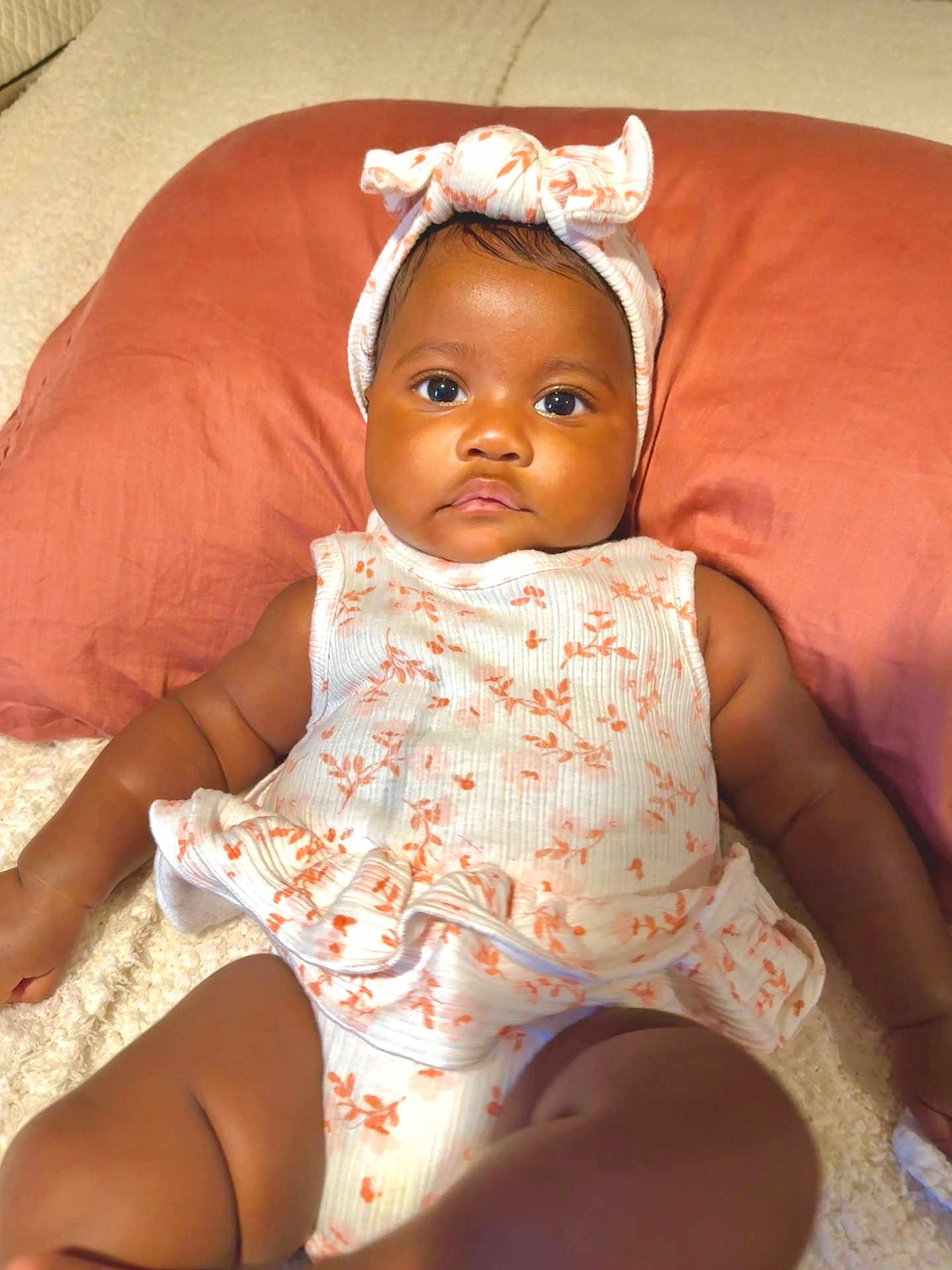 Nelliana joined the competition — help win amazing prizes! baby, infant, child, cute, headband, pillow, floral_outfit, lying_down, soft_surface, portrait, indoors, skin, face, arms, legs, closeup, serious_expression, clothing, headwear, adorable