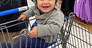 Trysten is registered to the contest to win money with this photo: toddler, shopping_cart, reindeer_antlers, smiling, child, store, clothing_rack, holiday_hat, indoor, person, happy, shopping, casual_clothing, retail, floor, footwear, adult, gray_jacket, blue_seat, festive