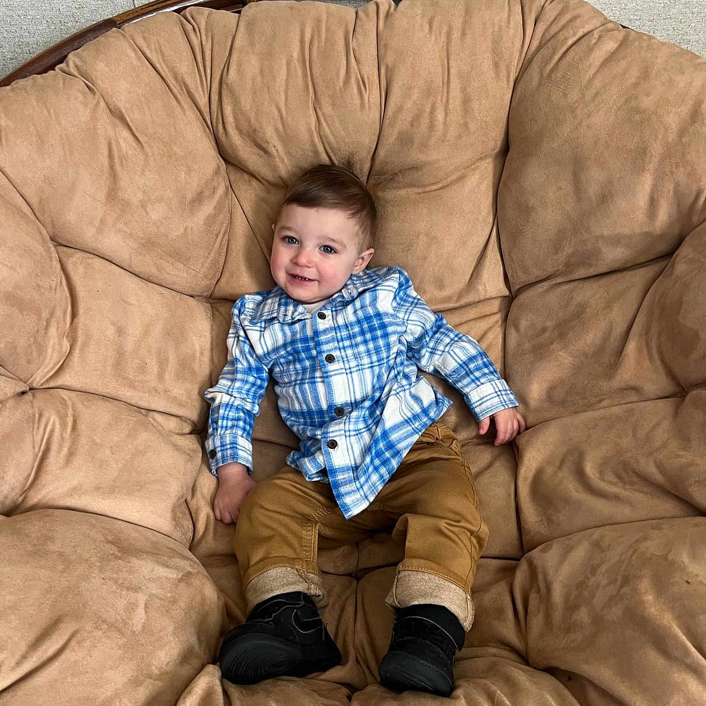 Trysten is registered to the contest to win money with this photo: toddler, child, plaid_shirt, brown_pants, black_shoes, cushioned_chair, indoor, smiling, happy, comfortable, seated, young_child, casual_clothing, cozy, furniture, portrait, cute, relaxed, baby, person