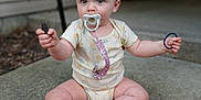 Amari is registered to the contest to win money with this photo: baby, child, pacifier, bow, onesie, sitting, outdoor, concrete, pavement, barefoot, hands, eyes, expression, toy, pacifier_clip, hair, legs, face, portrait, holding_stick