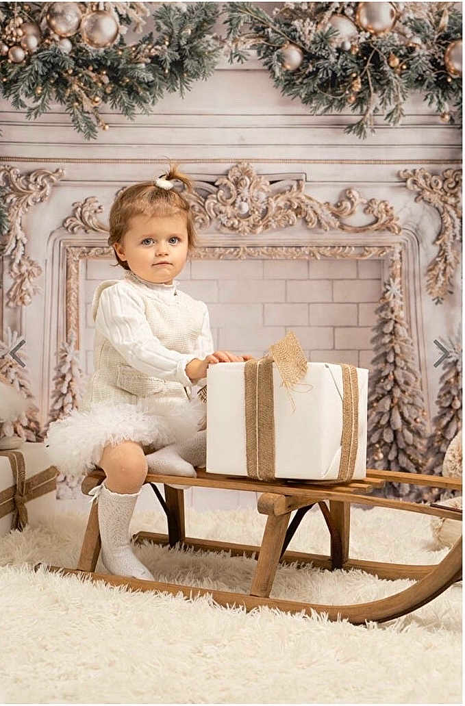 Eva participe au concours pour gagner de l'argent avec cette photo : toddler, child, sled, gift, white_clothing, knitwear, holiday_decor, ornaments, carpet, wooden_furniture, indoor, portrait, winter_theme, decorative_garland, cute, festive, present, sitting, expression, cozy