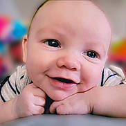 Cairo is registered to the contest to win money with this photo: baby, close_up, smile, face, hands, resting, child, cute, portrait, indoor, skin, eyes, expression, happy, infant, young, cheeks, casual_clothing, background_blur, colorful_background