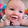 baby, close_up, smile, face, hands, resting, child, cute, portrait, indoor, skin, eyes, expression, happy, infant, young, cheeks, casual_clothing, background_blur, colorful_background