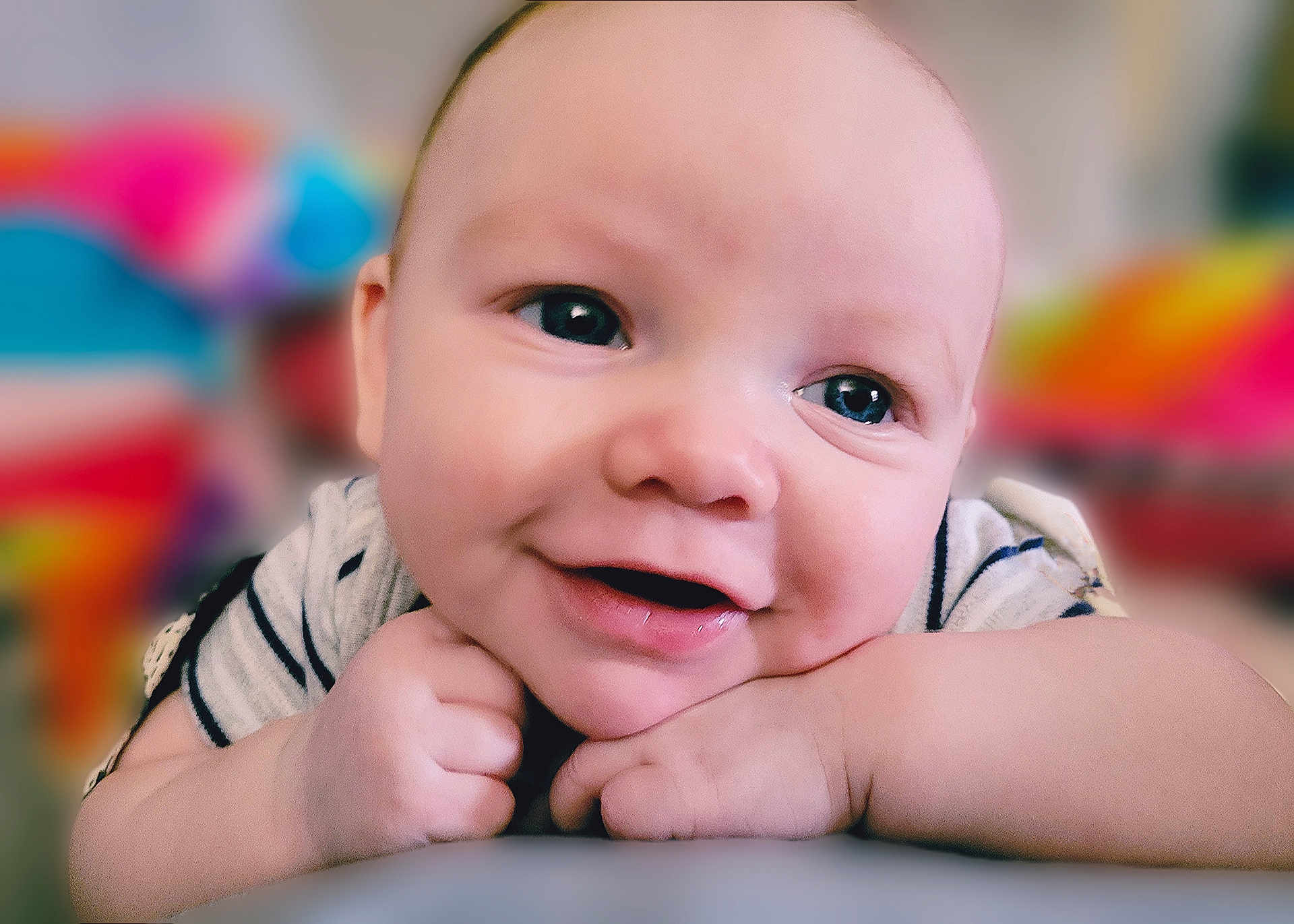 Cairo is registered to the contest to win money with this photo: baby, close_up, smile, face, hands, resting, child, cute, portrait, indoor, skin, eyes, expression, happy, infant, young, cheeks, casual_clothing, background_blur, colorful_background