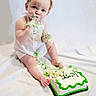 Cairo is registered to the contest to win money with this photo: baby, child, cake, messy, apron, curly_hair, smiling, sitting, white_background, green_icing, birthday, fingers, feet, celebration, food, happy, portrait, face, cute, infant