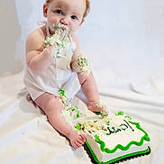 Cairo is registered to the contest to win money with this photo: baby, cake, cake_smash, curly_hair, frosting, infant, messy, white_background, sitting, cute, red_hair, birthday, food, hands, face, foot, apron, celebration, smiling, young_child