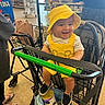 baby, child, shopping_cart, yellow_hat, yellow_outfit, smile, grocery_store, person, footwear, can, bag, shopping, clothing, happy, indoor, retail, store_shelves, people, casual, infant