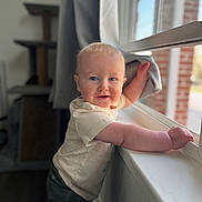 Jared is registered to the contest to win money with this photo: baby, bodypart, clothing, dress, face, finger, hand, happy, head, pants, person, photography, portrait, shorts, sitting, smile, t_shirt, window, windowsill, wood