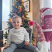 Ayden participe au concours pour gagner de l'argent avec cette photo : child, toddler, baby, christmas_tree, ornament, lights, chair, armchair, gnome, plush, festive, holiday, smile, sweater, socks, living_room, decoration, portrait, happy, indoor