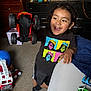 Izayah is registered to the contest to win money with this photo: child, toy_truck, smiling, indoor, carpet, toy_fire_truck, shorts, tshirt, happy, playing, boy, furniture, blanket, table, toy_cars, black_socks, cabinet, room, hair, face