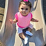 toddler, child, slide, playground, pink_bow, pink_bib, curly_hair, white_shoes, sunlight, shadow, outdoor, play, cute, baby, sitting, happy, park, clothing, person, smile