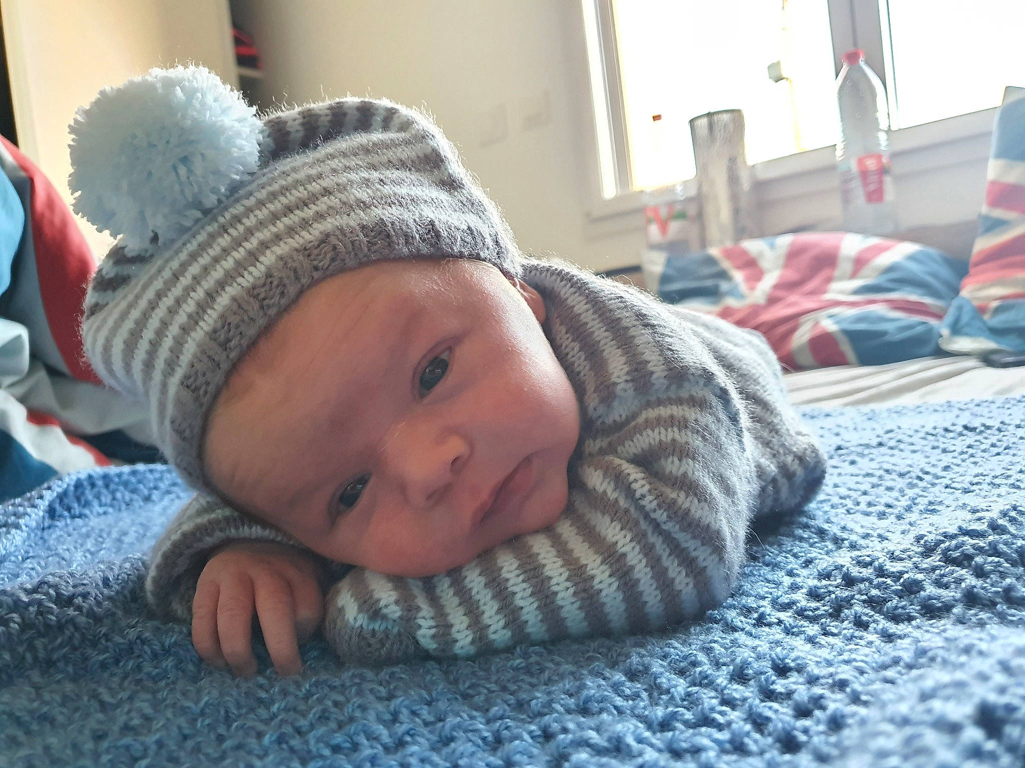 Axel a rejoint le concours — aidez-le/la à gagner de superbes lots ! baby, baby_toddler_clothing, cap, cheek, child, chin, comfort, eye, flooring, grey, headwear, knit_cap, linens, nose, person, room, sitting, skin, smile, toddler