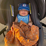 Samuel joined the competition — help win amazing prizes! baby, blue_cap, orange_blanket, stroller, smiling, outdoor, child, tank_top, sunlight, happy, infant, person, blanket, cute, seat, clothing, headwear, warm_light, baby_face, comfort