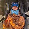 baby, blue_cap, orange_blanket, stroller, smiling, outdoor, child, tank_top, sunlight, happy, infant, person, blanket, cute, seat, clothing, headwear, warm_light, baby_face, comfort