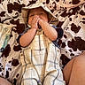 baby, infant, plaid_clothing, hat, blanket, cow_print, hand, face, lying_down, wipes, package, skin, cute, playful, child, indoors, soft_lighting, person, smiling, comfortable