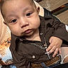 Samuel joined the competition — help win amazing prizes! baby, child, person, face, hand, jewelry, cross_necklace, brown_shirt, jeans, belt, wooden_bench, curious_expression, closeup, sitting, casual_clothing, indoor, portrait, cute, accessory, infant