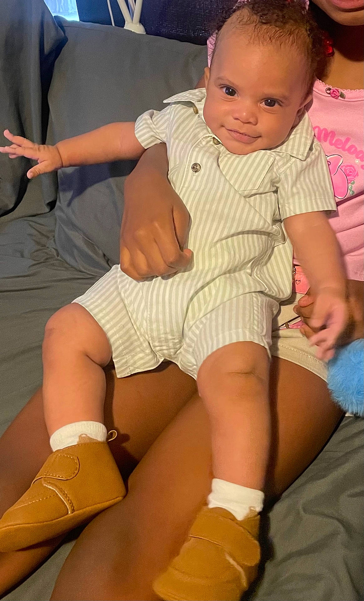 Jahmir is registered to the contest to win money with this photo: baby, child, clothing, cute, face, footwear, hand, happy, indoor, infant, lap, person, pink, romper, shoes, sitting, skin, smile, striped, toy