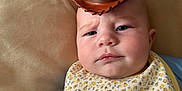 Rayne is registered to the contest to win money with this photo: baby, cowboy_hat, bib, floral_pattern, cushion, indoor, portrait, child, blue_shirt, facial_expression, serious, headwear, person, skin, closeup, infant, cute, young_child, resting, home