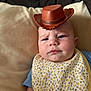 baby, cowboy_hat, bib, floral_pattern, cushion, indoor, portrait, child, blue_shirt, facial_expression, serious, headwear, person, skin, closeup, infant, cute, young_child, resting, home